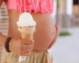 Schwanger und Lust auf Eis? Eine Frau hält eine Eistüte, während sie ihren Bauch streichelt.