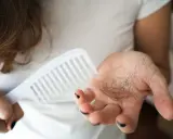 Frau hält Kamm und Haarbüschel in der Hand. Ein häufiges Problem: 4 Monate nach Geburt Haarausfall.