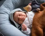 Ein Neugeborenes schläft friedlich in einer Babywippe, eingewickelt in eine warme Decke. Vielleicht ist es der 37 wochen schub, der ihm süße Träume schenkt.