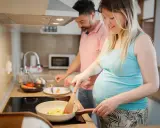 Schwangere Frau kocht Rührei, während ihr Mann daneben steht. Sie achtet auf ihre Ernährung, um Listeriose in der Schwangerschaft zu vermeiden.