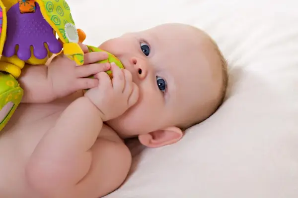 Ein Baby mit blauen Augen erkundet sein buntes Spielzeug. Vielleicht ist es der 19-Wochen-Schub, der ihn so neugierig macht.