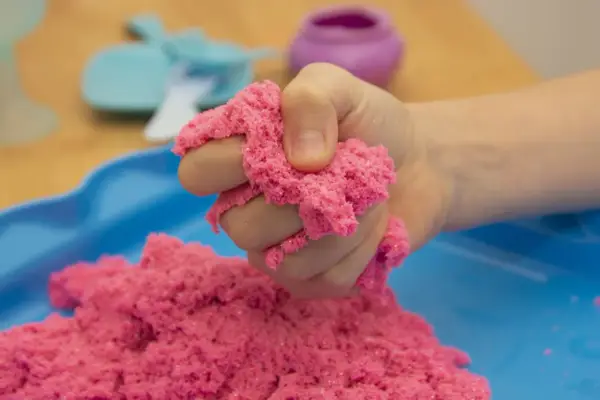 Kind hält pinken kinetischen Sand, der sich leicht formen lässt. Perfekt zum **kinetic sand selber machen** und Spielen.